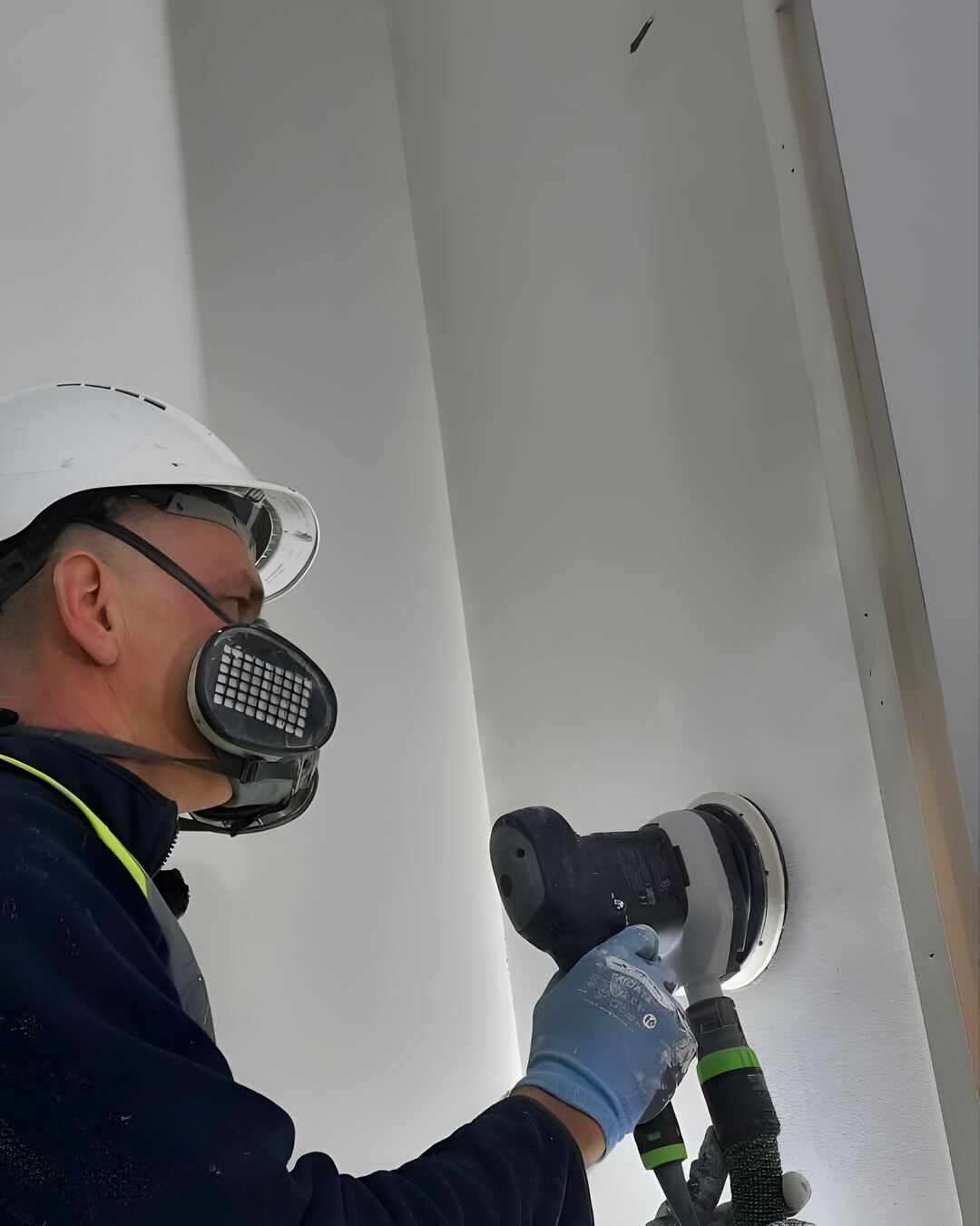 Vitalii in a hard hat and dust mask, skimming a wall on site
