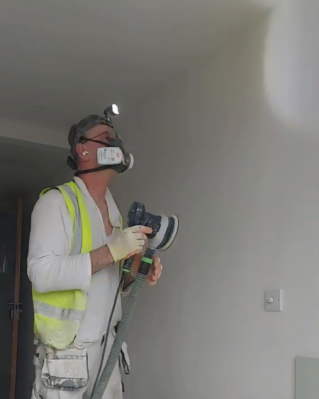 Vitalii in a dust mask and head torch, sanding a wall at New Eidyn
