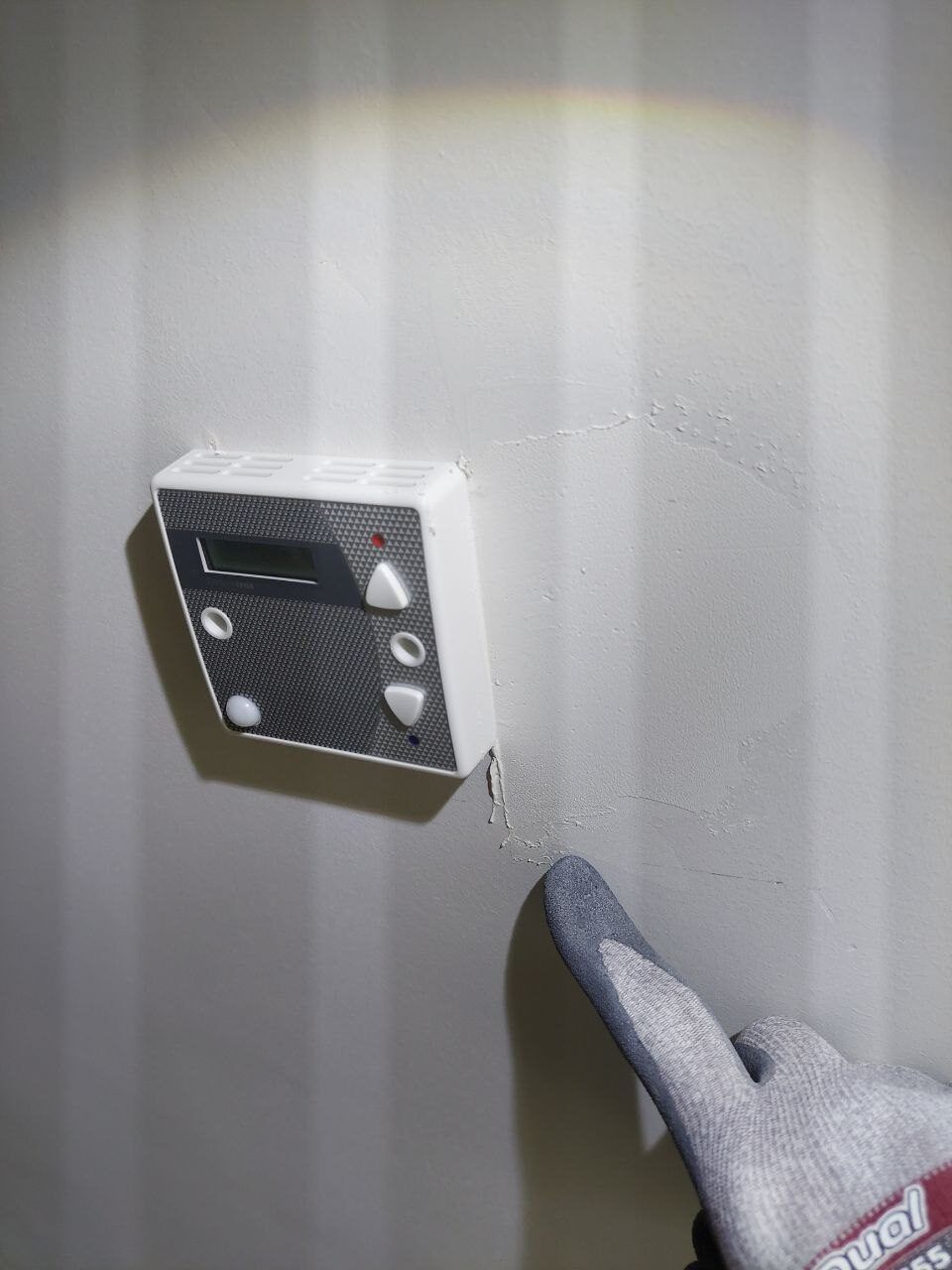 A gloved finger pointing out a crack beside a wall controller during a snag walkthrough